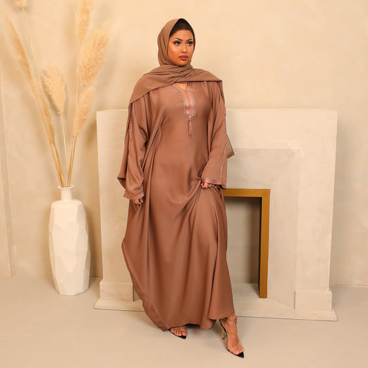Woman wearing a brown abaya in a minimalistic setting with a vase and fireplace.